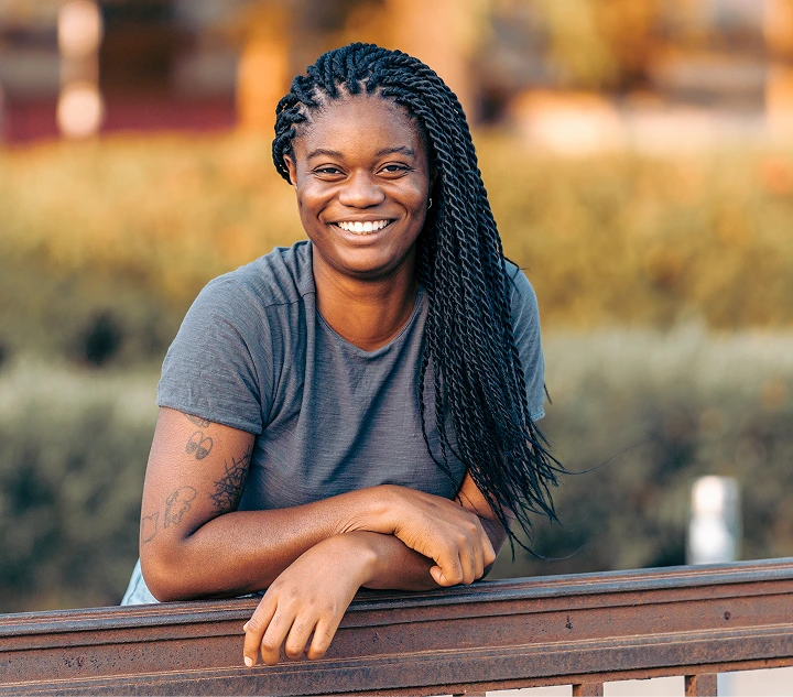 Woman smiling at camera leaning on wooden railing in outdoor setting