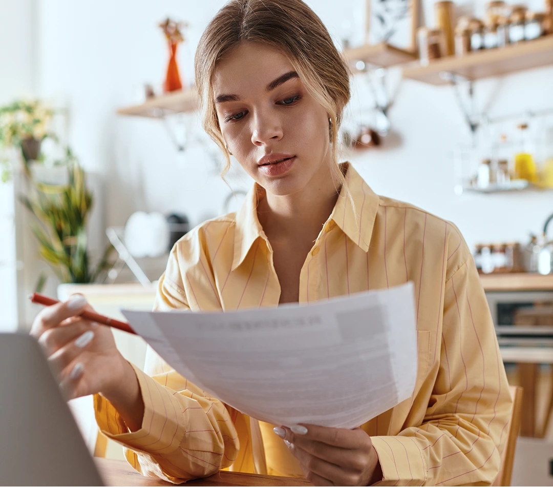 Woman in yellow shirt reviewing documents at a kitchen table