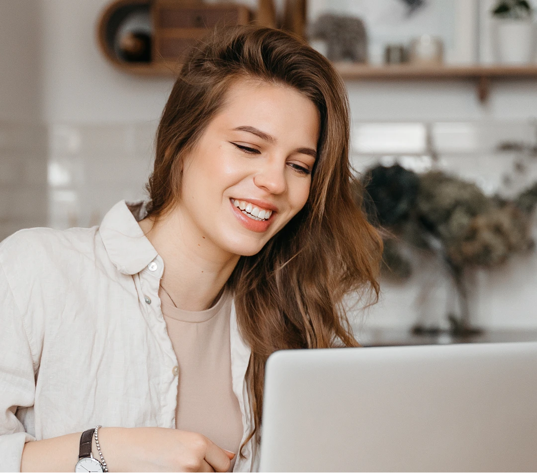 Woman smiling while viewing laptop screen in a bright home office