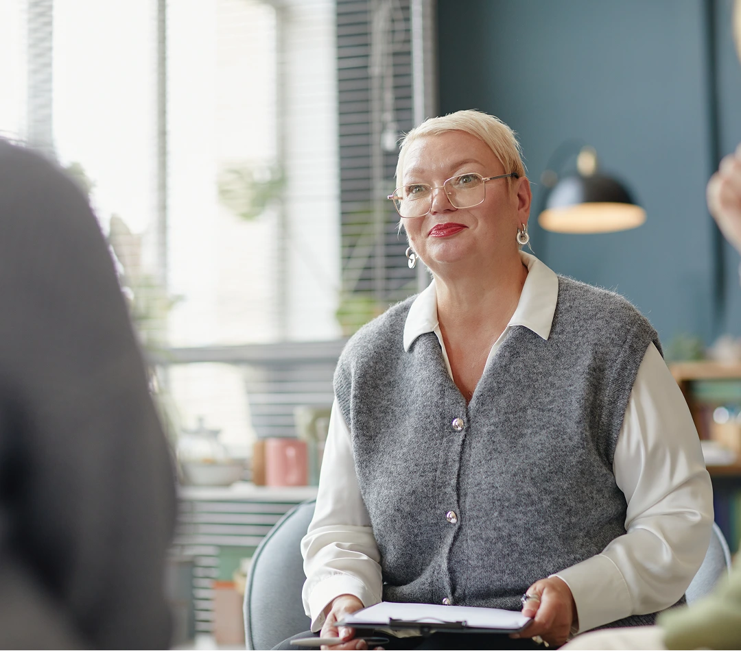 Psychologist in glasses and gray vest conducting a therapy session with a patient in a bright office