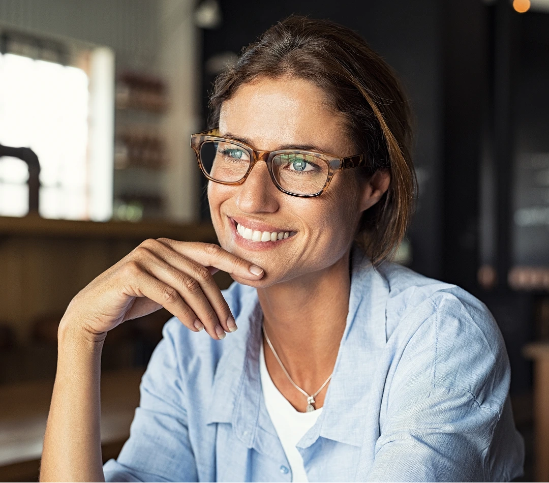 Woman wearing glasses and blue shirt smiling in a clinical office setting