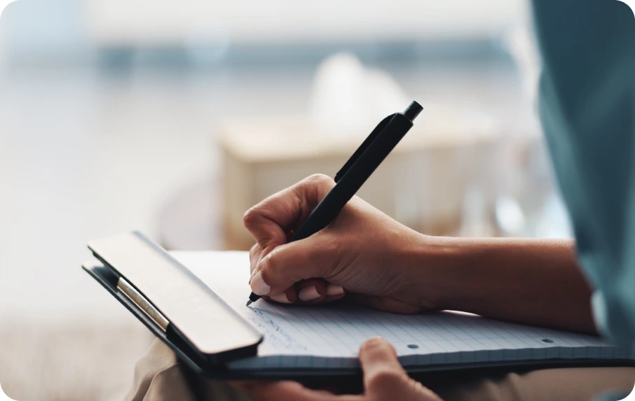 Person writing on a form with a pen while holding a clipboard