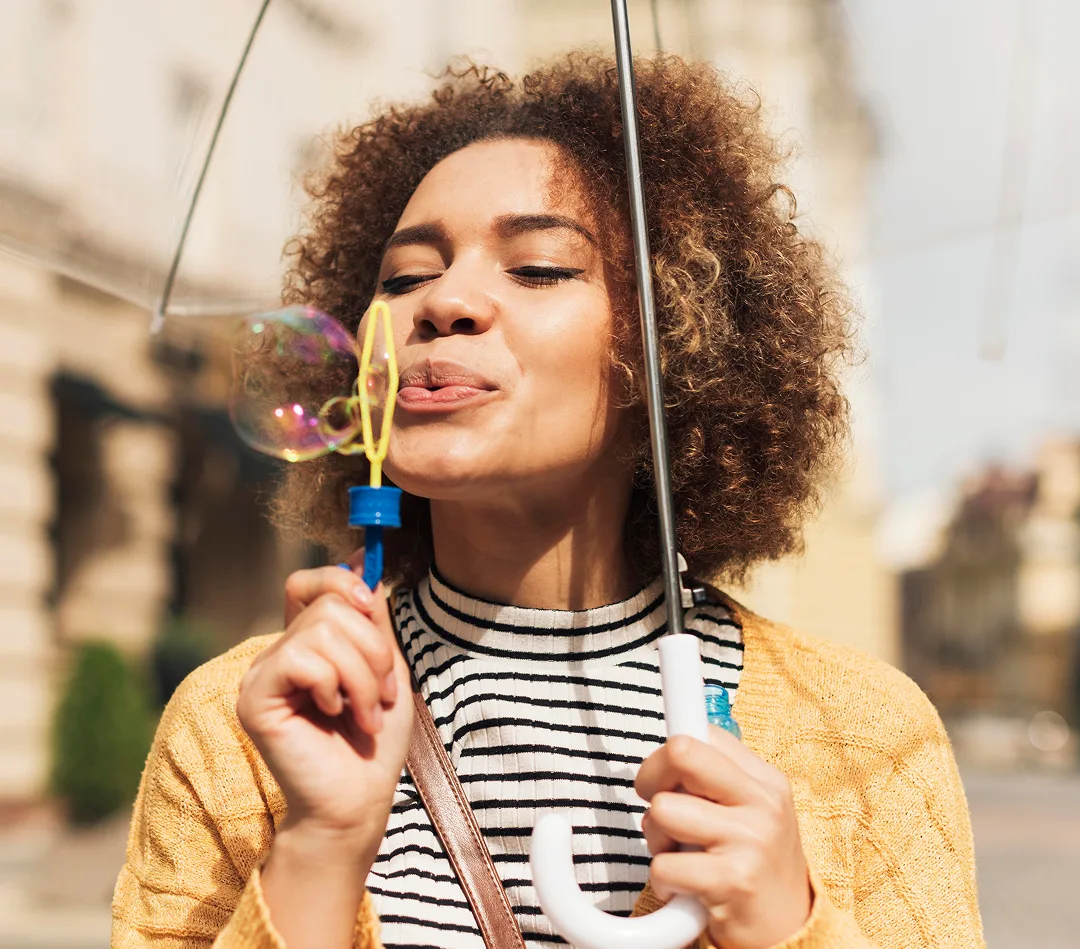 Person blowing bubbles outdoors while holding a bubble wand