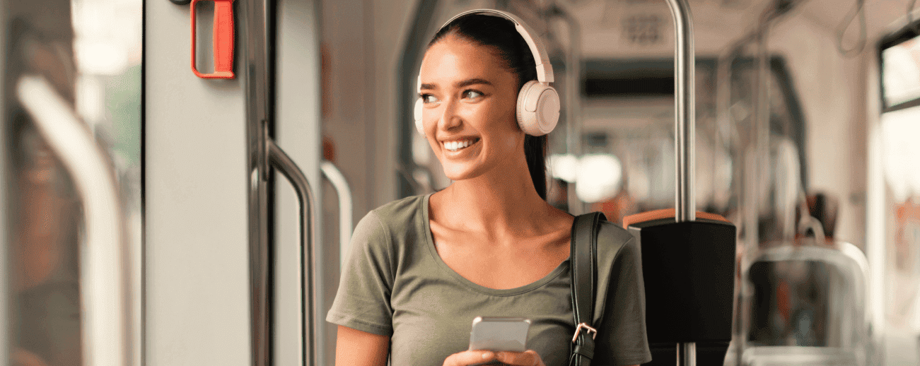 Smiling woman wearing white headphones and holding a phone on public transit