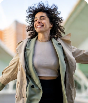 Smiling woman with curly dark hair wearing a beige jacket outdoors