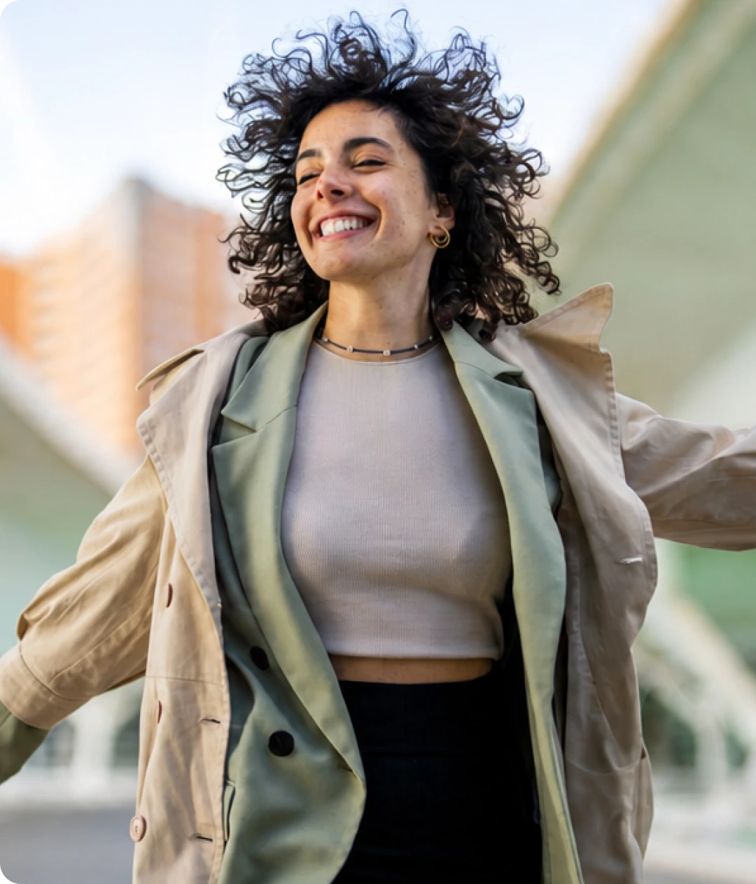 Smiling woman with curly dark hair outdoors wearing a beige blazer
