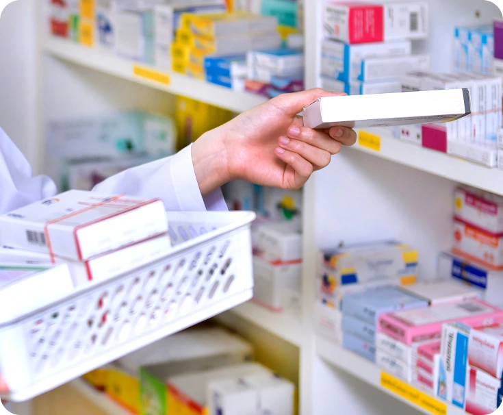 Pharmacist selecting medication box from shelf stocked with colorful pharmaceutical packages