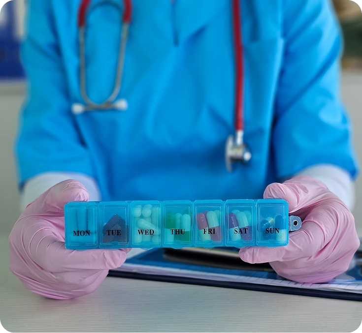Healthcare provider in blue scrubs holding a blue weekly pill organizer with pink gloved hands