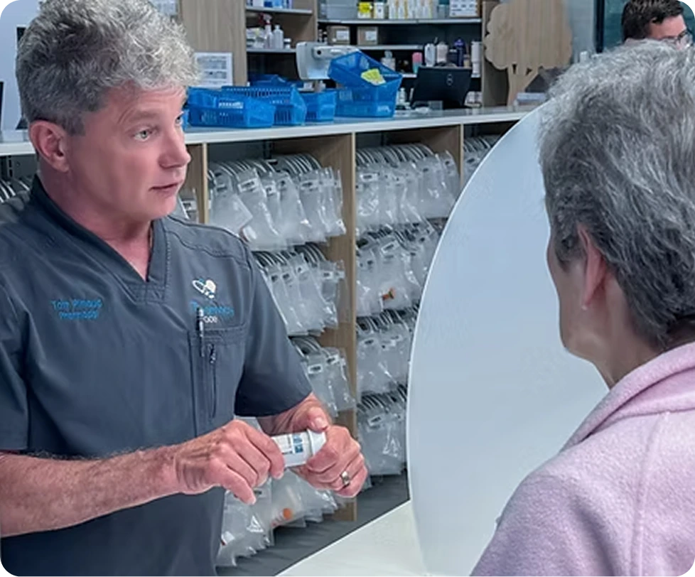 Pharmacist handing medication bottle to customer in pharmacy with organized medication shelves