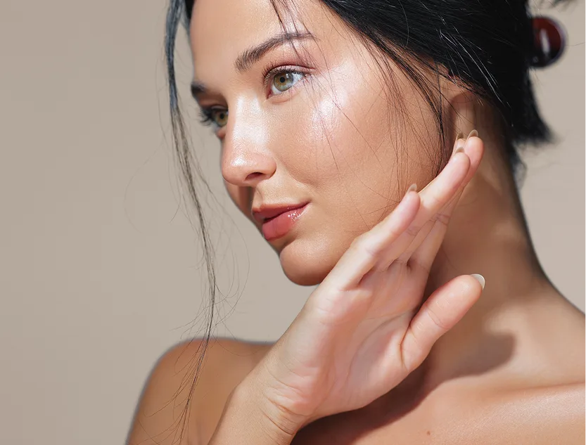 Woman with radiant skin touching her face in profile against neutral background