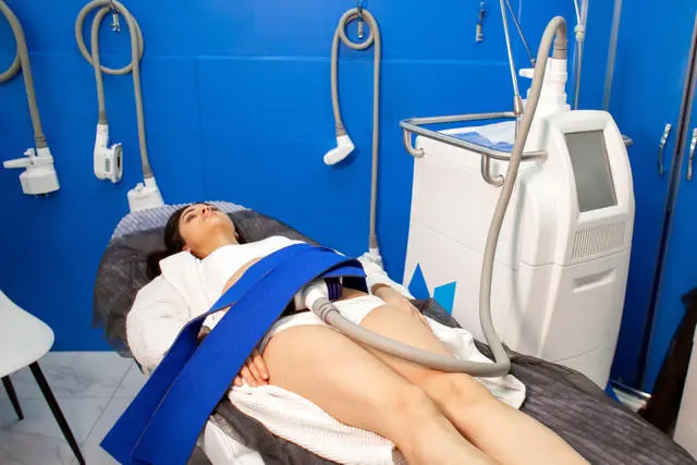 Patient receiving CoolSculpting treatment on abdomen with applicator applicator against blue-walled treatment room background