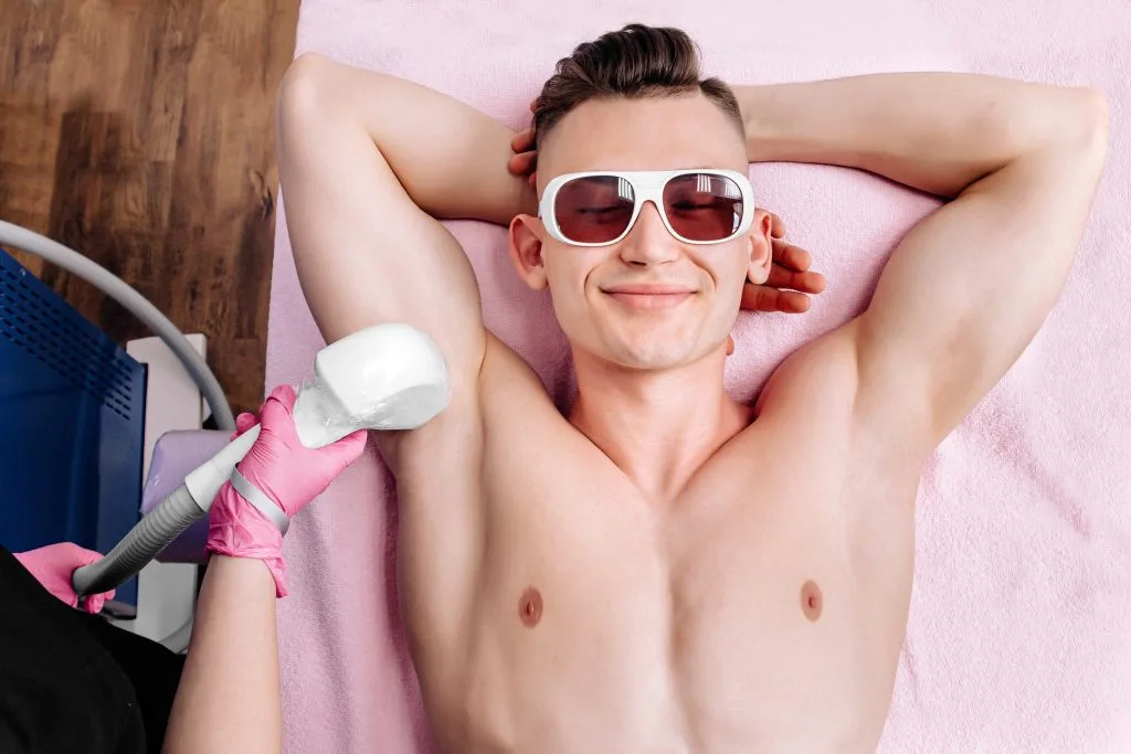 Man receiving laser hair removal treatment on his chest from technician wearing pink gloves