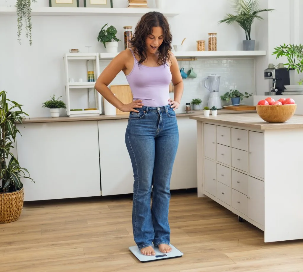 Woman standing on scale in modern kitchen, checking her weight