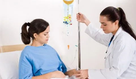 Healthcare provider adjusting IV drip line for patient seated in treatment chair