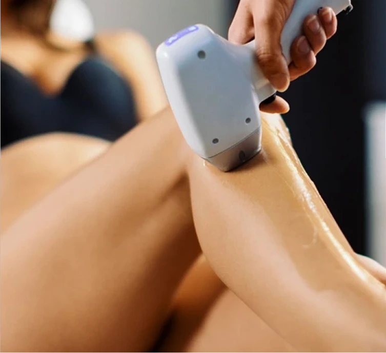 Technician applying handheld laser hair removal device to patient's leg