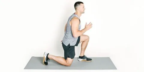 Man performing a plyometric lunge on a gray exercise mat indoors