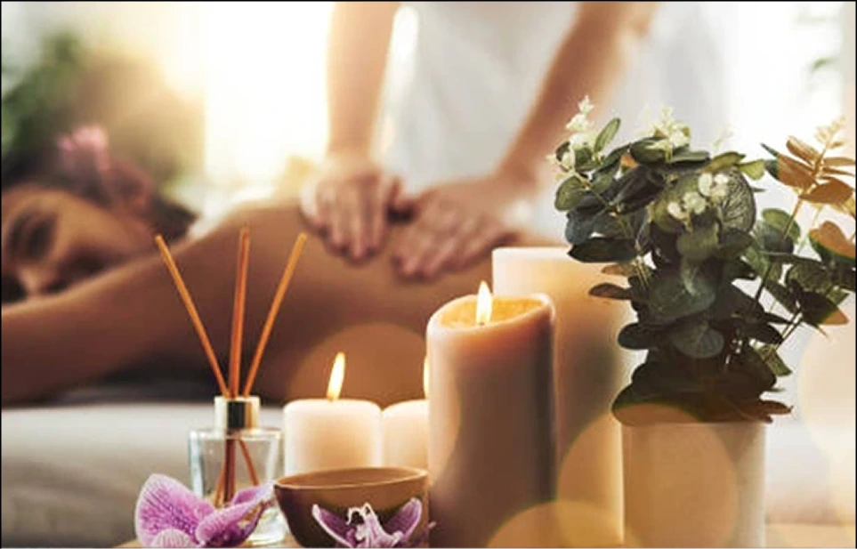 Therapist performing massage on client's back with candles, diffuser, and plants on nearby table