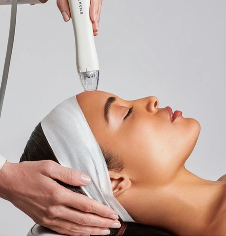 Practitioner using Syma microneedling device on patient's forehead and cheek