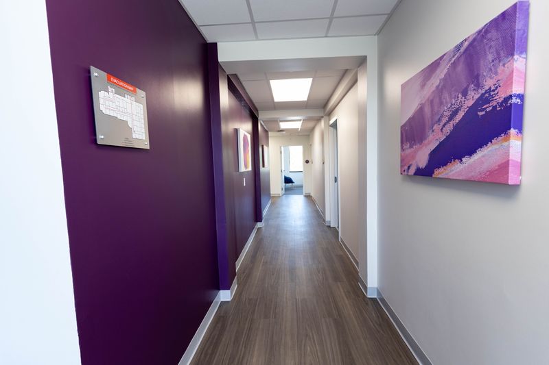 Corridor with deep purple accent wall, abstract pink and purple artwork, and glass window to adjacent room
