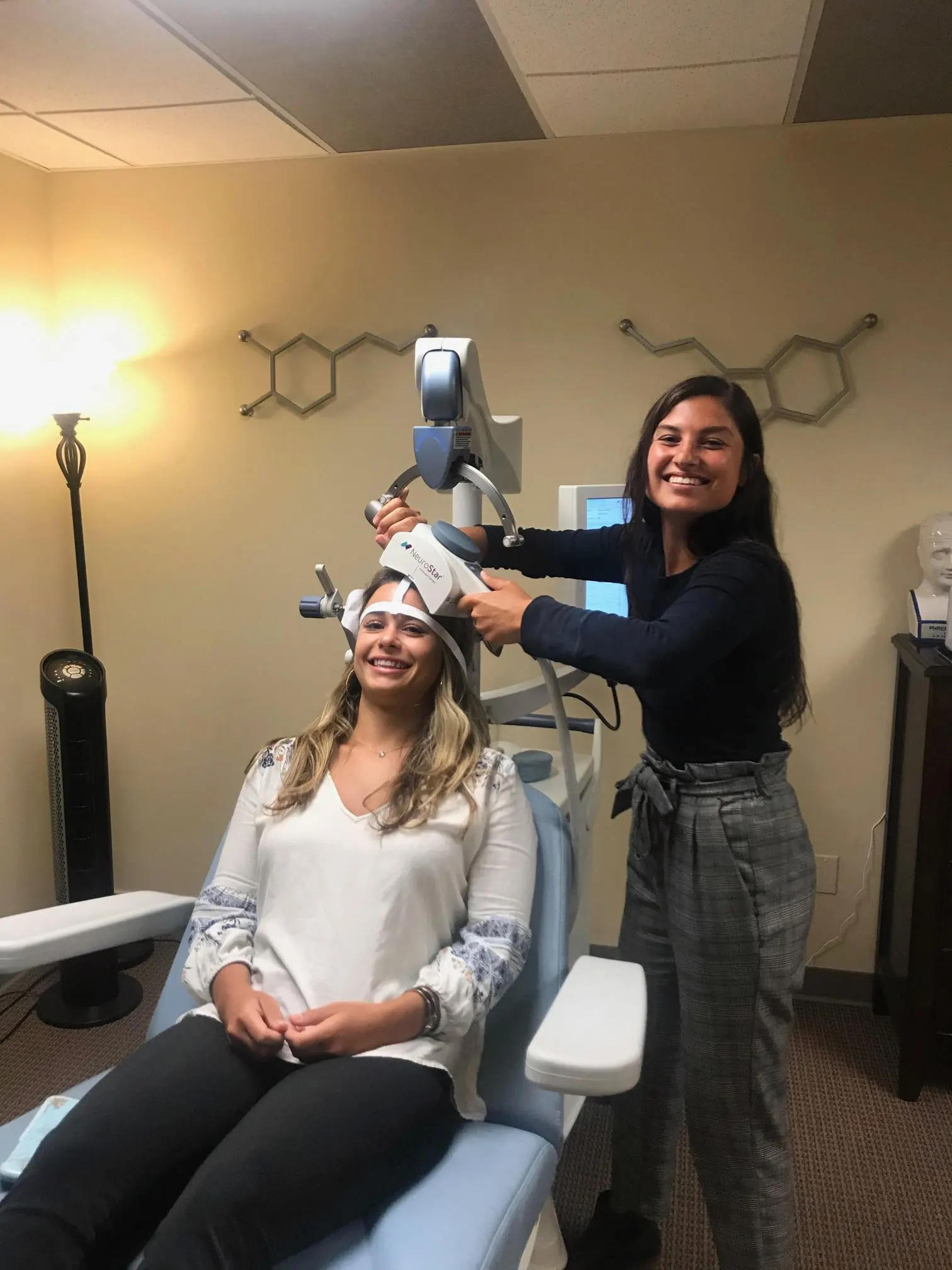 Staff member placing NeuroStar TMS magnetic coil on smiling patient's head in treatment room