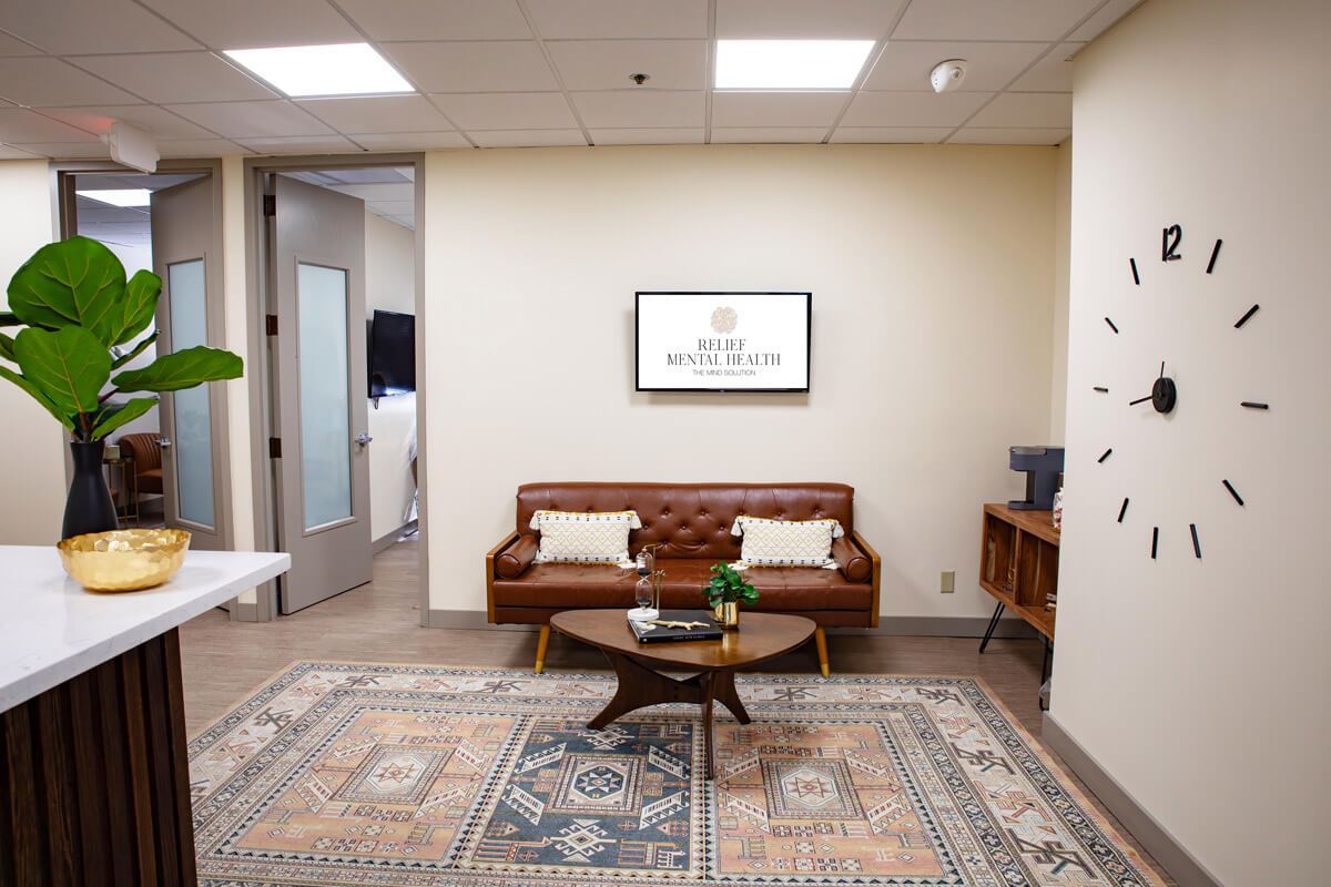 Relief Mental Health clinic waiting room with brown leather sofa, round coffee table, potted plant, wall clock, and logo on wall