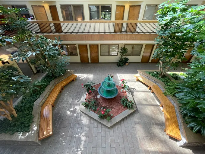 Indoor atrium with two-story wooden railings, plants, and central water fountain with seating areas
