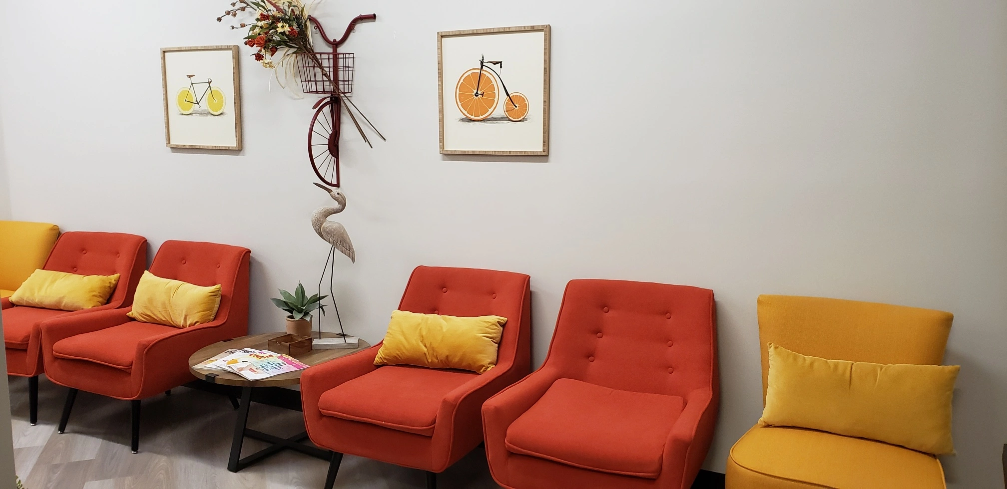 Waiting area with red and yellow seating, framed citrus and geometric artwork, decorative branches and plants, small side table