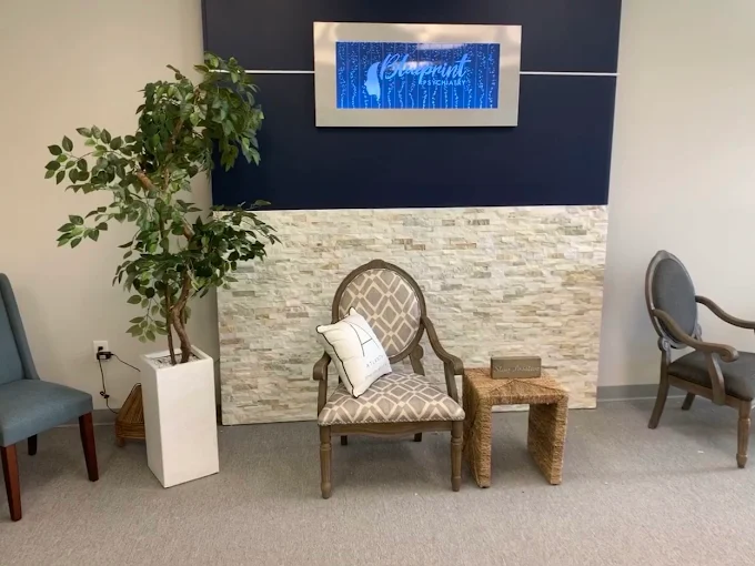 Waiting room with upholstered chairs, potted plant, stone accent wall, and blue sign