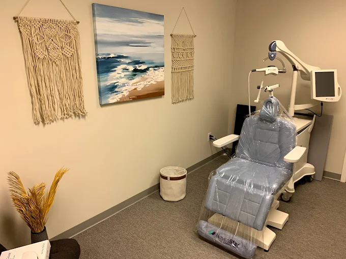 TMS treatment room with therapeutic device, coastal artwork, macram&eacute; wall hangings, and decorative plants