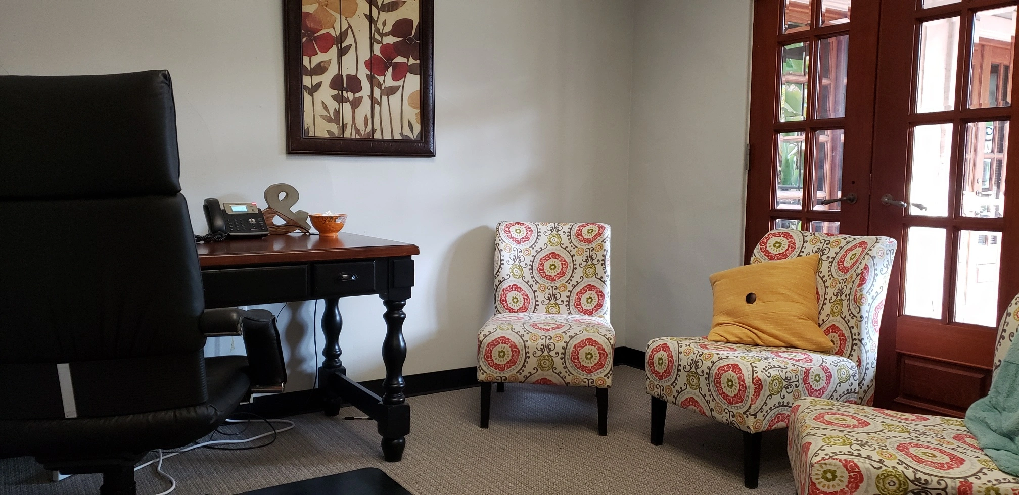 TMS therapy office lounge with patterned accent chairs, desk, artwork, and wooden doors