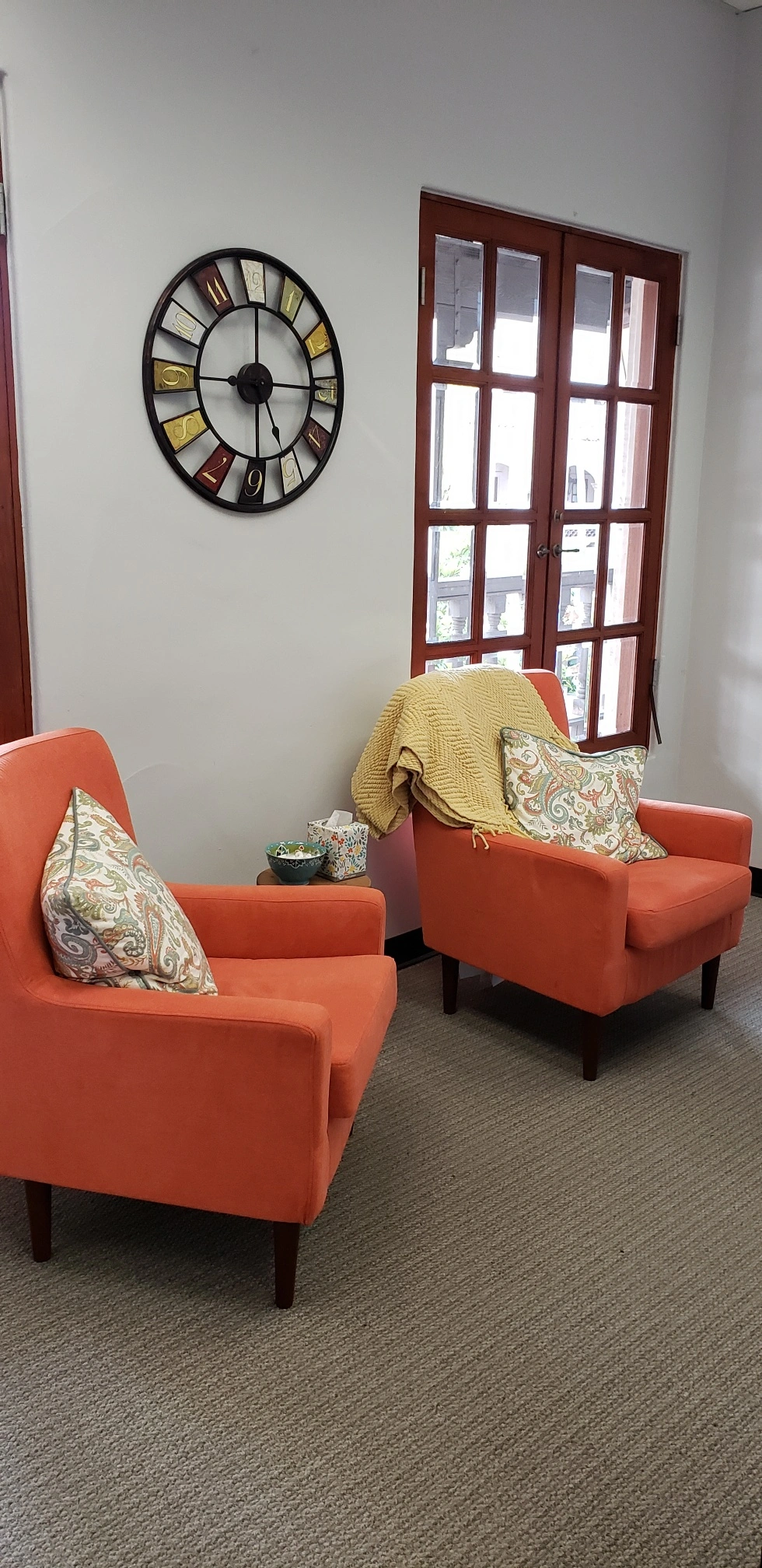 Waiting room with two orange armchairs, decorative clock, and French doors opening to outdoor area