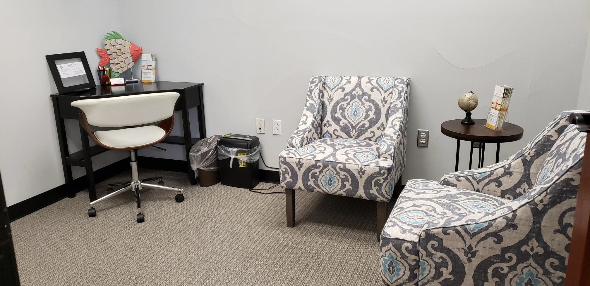 TMS therapy office waiting area with patterned armchairs, desk with computer, and side table with decorative items