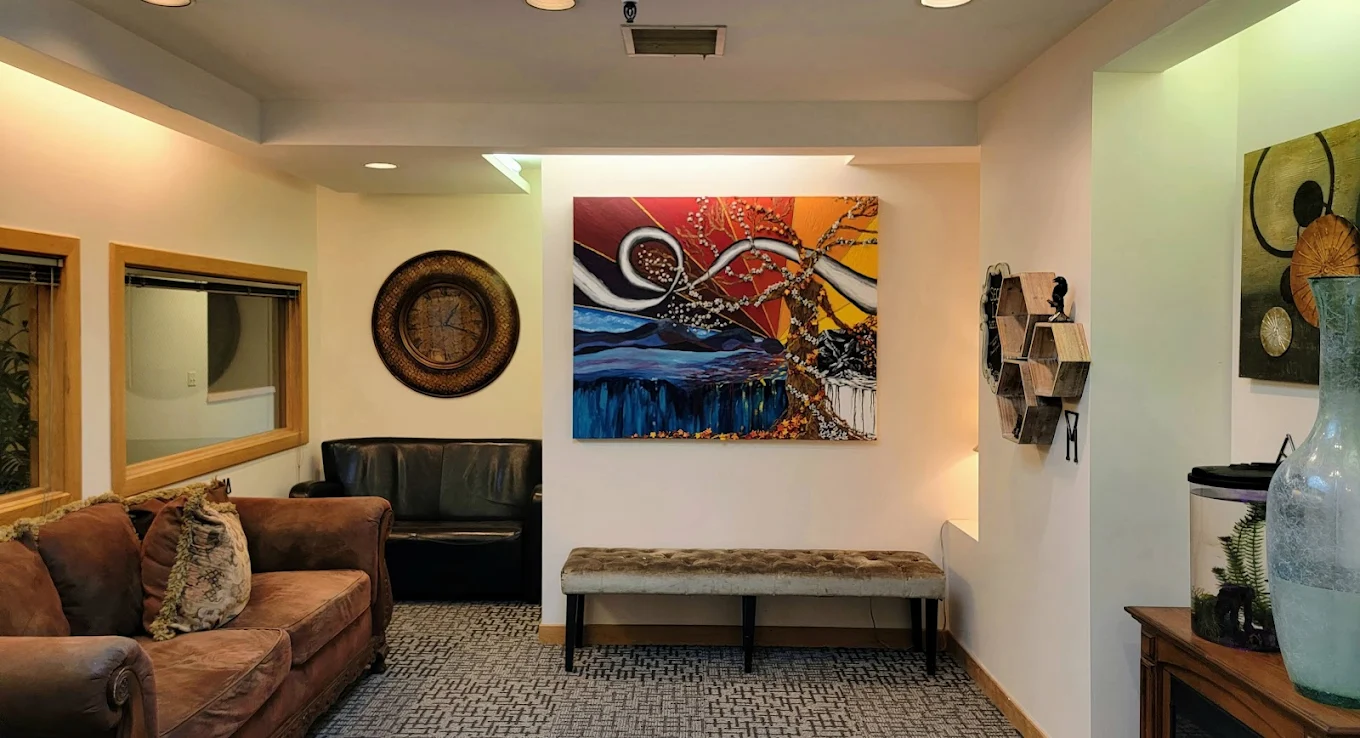 Comfortable waiting room with rust-colored sofa, black chairs, colorful abstract art, and decorative accents
