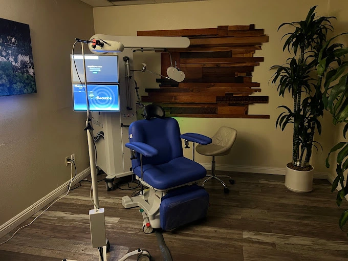 TMS treatment room with blue patient chair, medical display screens, and overhead coil apparatus