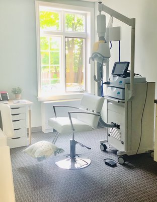 TMS therapy treatment room with equipment mounted overhead and patient chair by bright window