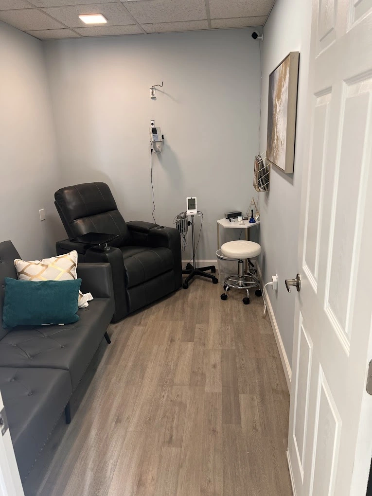 TMS therapy treatment room with black reclining chair, IV stand, small white stool, and medical equipment on white walls