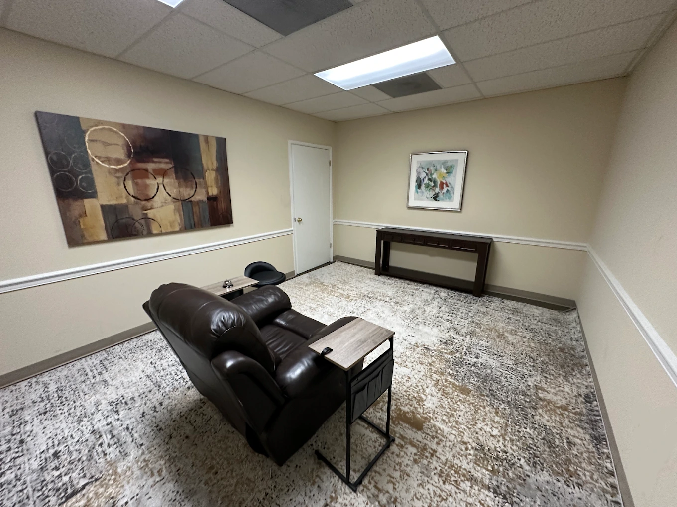 TMS therapy room with black leather reclining chair, abstract wall art, and framed botanical print