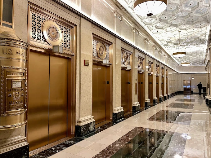 Historic building hallway with rows of brass elevator doors and ornate architectural details