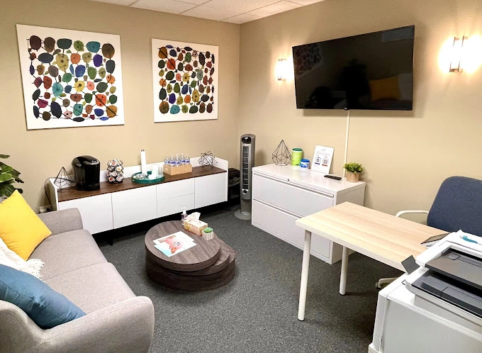 TMS therapy office waiting room with colorful abstract artwork, white furniture, TV, and comfortable seating