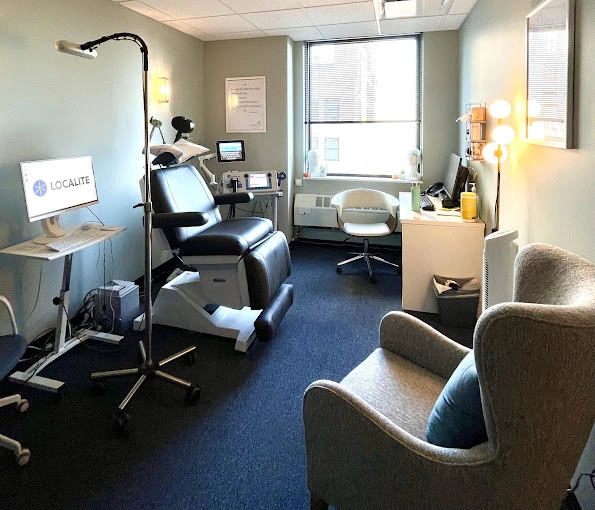 TMS treatment room with black patient chair, treatment coil apparatus, monitor, and gray waiting chairs