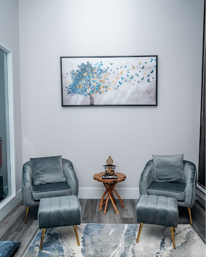 Waiting room with two gray armchairs, wooden side table, and abstract tree artwork on white wall