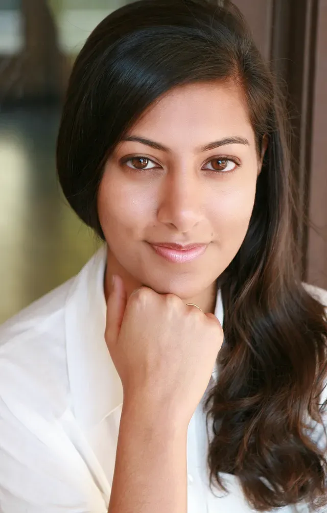 Portrait of a woman with long dark hair smiling, wearing a white top
