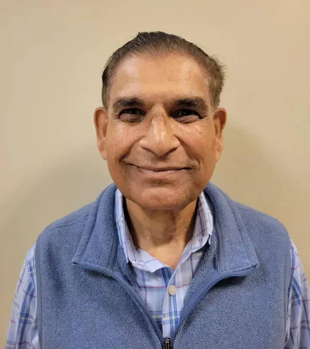 Portrait of a man smiling at the camera wearing a blue vest and checkered shirt
