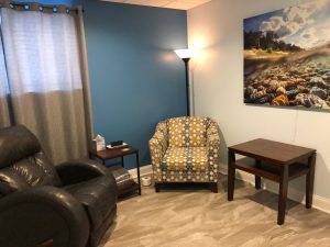 Patient relaxation room with blue accent wall, patterned armchair, leather sofa, and landscape artwork