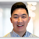 Man smiling in light blue collared shirt against blurred background