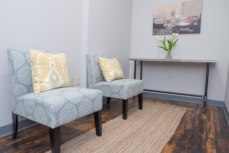 Therapy waiting room with two upholstered chairs, console table with flowers, and landscape artwork