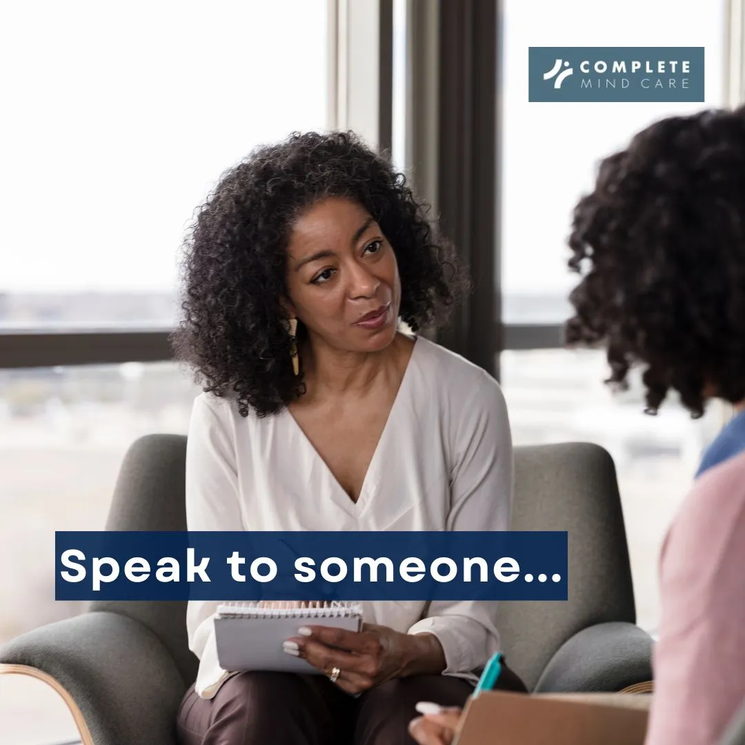 Mental health professional holding tablet speaking with patient in office, Complete Mind Care logo visible