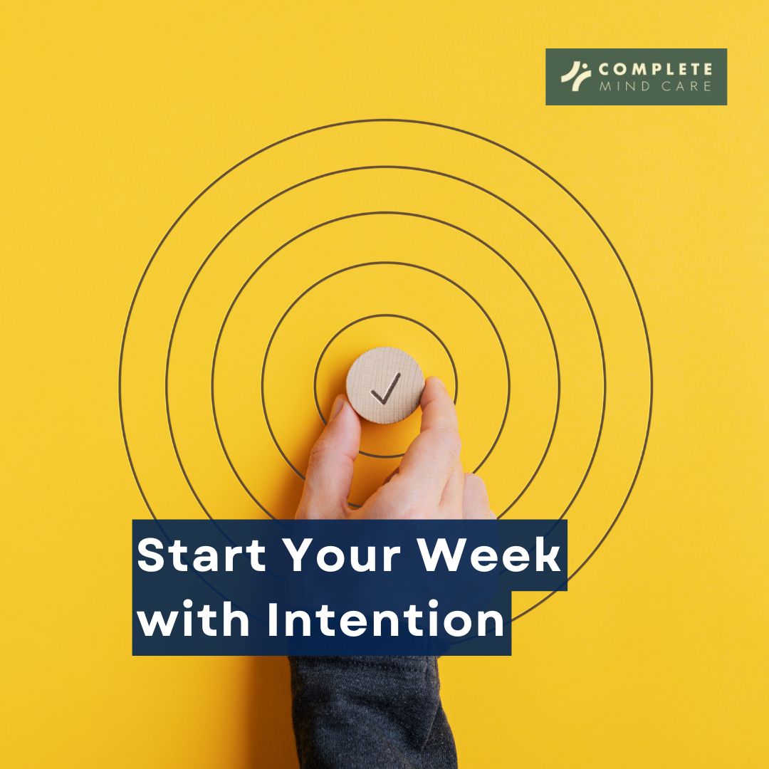 Hand holding wooden disc with checkmark over concentric circles on yellow background, text reads Start Your Week with Intention