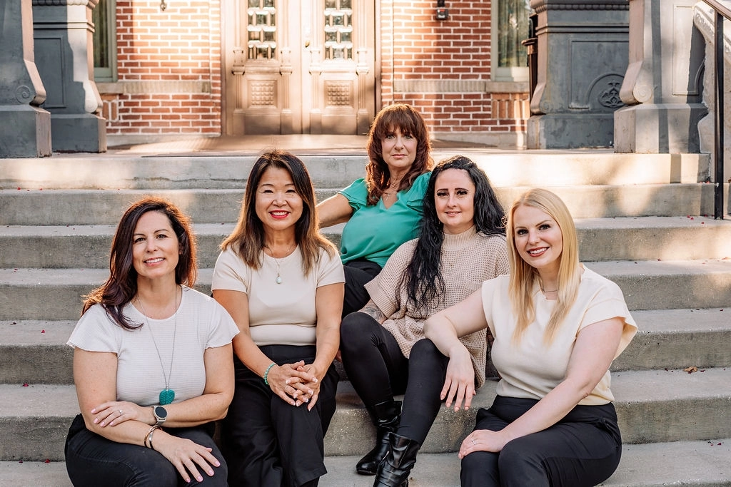 Five women posing together on brick building steps in afternoon sunlight