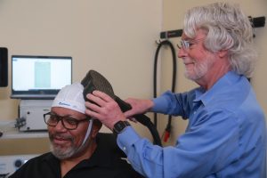 Clinician adjusting TMS coil on male patient's head with treatment equipment visible behind